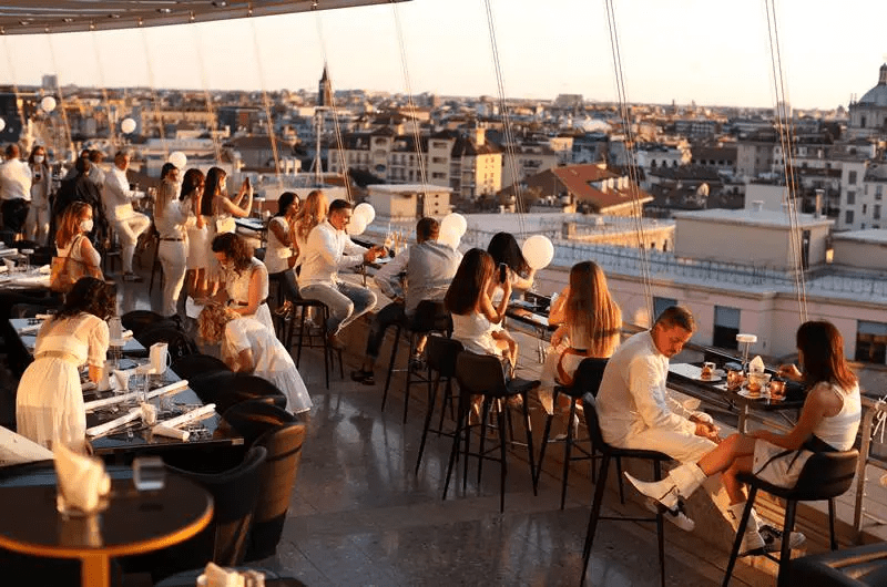 Persone vestite di bianco che fanno aperitivo sulla terrazza The roof Milano con vista sui tetti della città