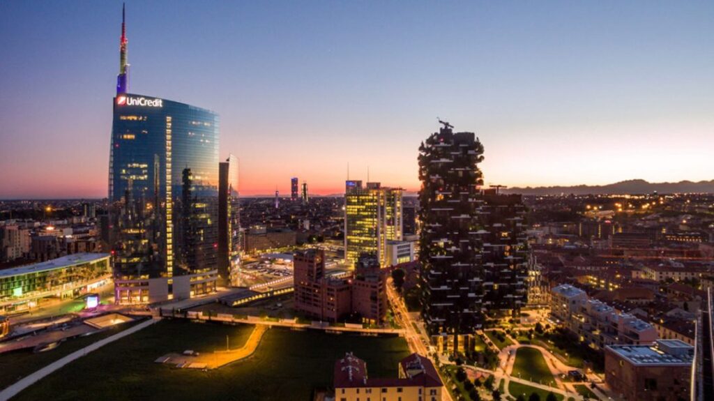 foto del quartiere di Isola a Milano dall'alto, di sera con le strade illuminate. In primo piano la Torre Unicredit e il Bosco Verticale.