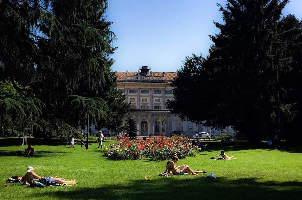 Parco all'interno dei giardini di Indro Montanelli. Le persone sul prato prendono il sole, sullo sfondo il palazzo reale. 