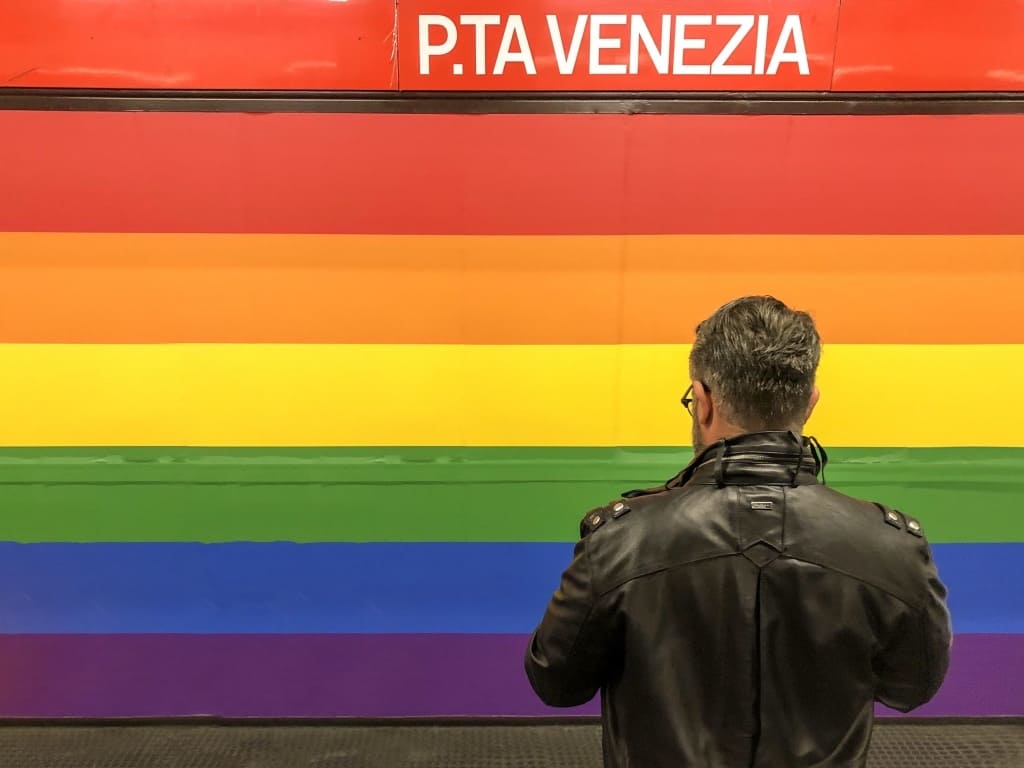 Fermata della metropolitana di Porta Venezia, colorata con i colori dell'arcobaleno. Un signore di spalle in primo piano. 