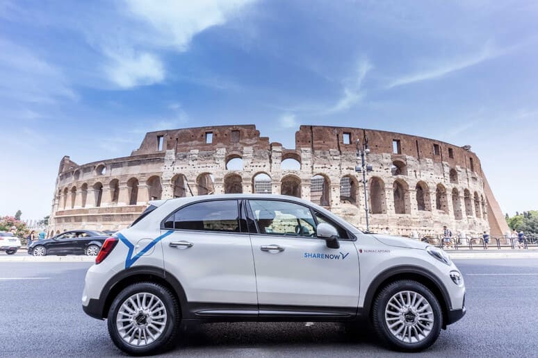 Fiat 500X bianca parcheggiata di fronte al Colosseo, con logo Sharenow.