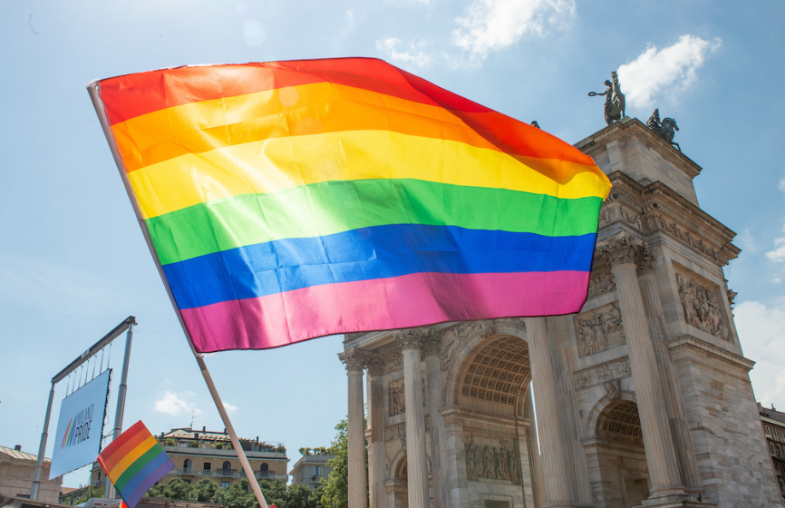  la bandiera arcobaleno in primo piano, sullo sfondo l’arco della pace